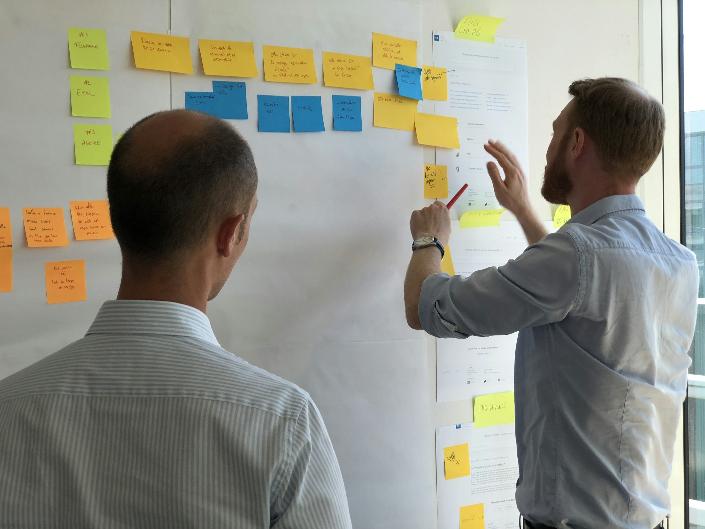 Team redesigning a go-to-market strategy at a wall of sticky notes Team redesigning a go-to-market strategy at a wall of sticky notes