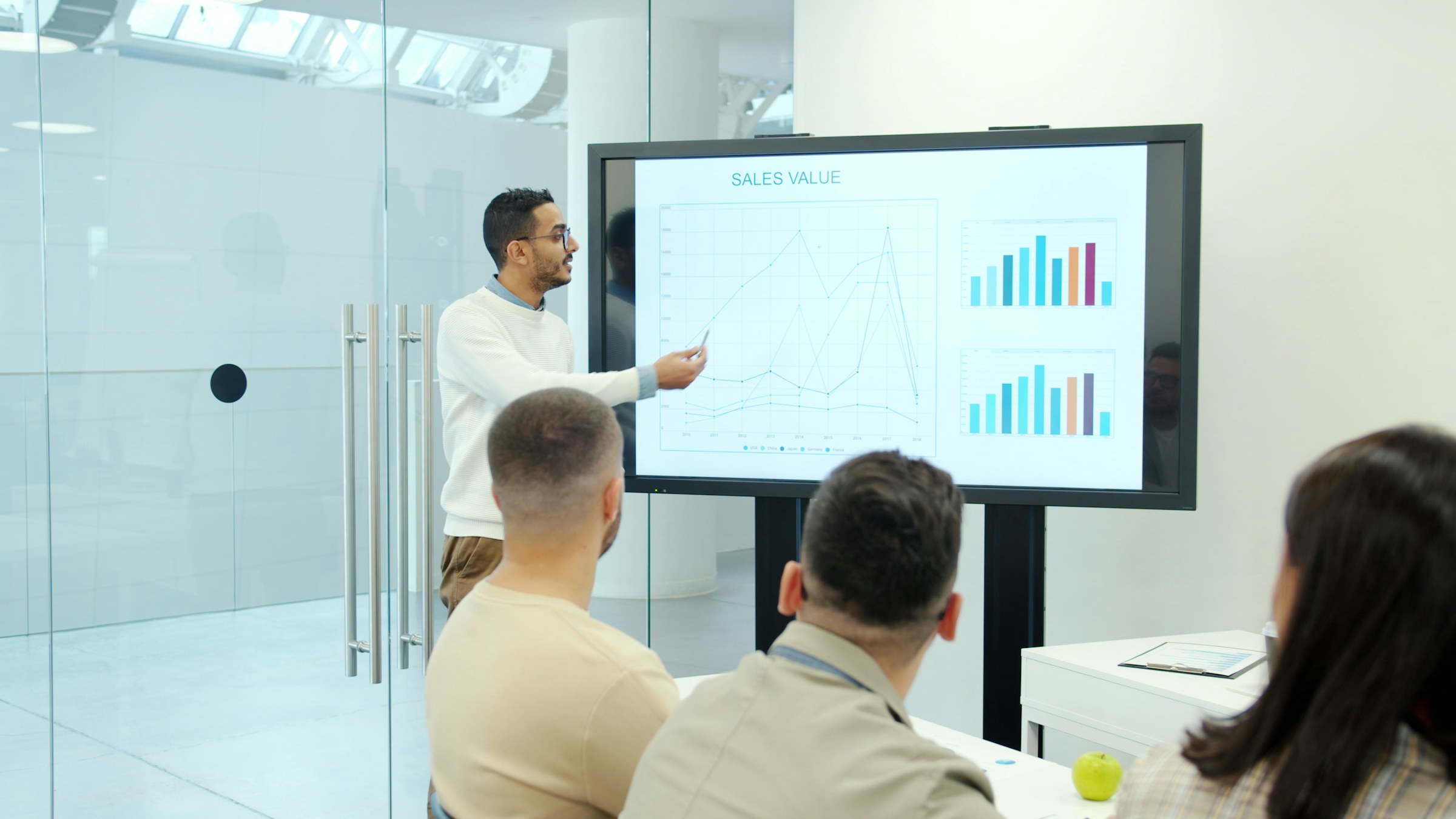 Consultant presenting market analysis charts on a large screen to a working group